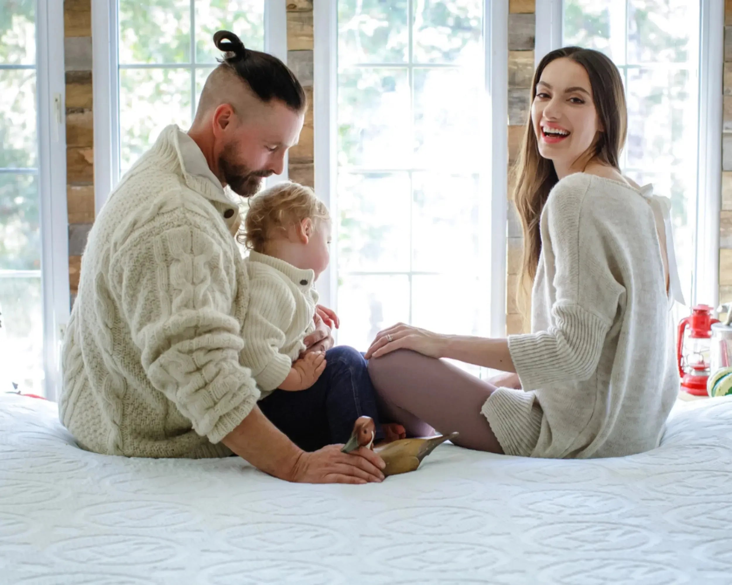 Family with mom, dad and child sitting on a Hiber mattress with a cabin background. 